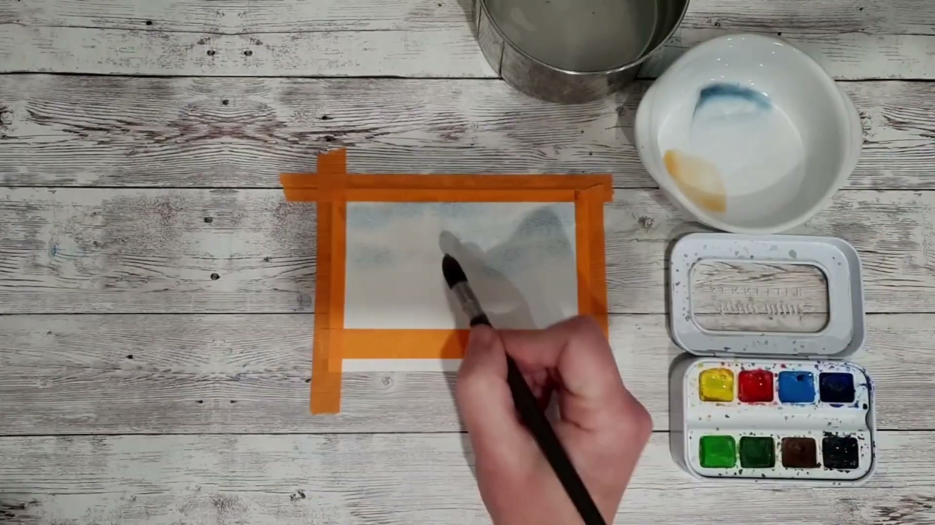 Application du mélange jaune de Naples (geogalium) et rouge sur le papier mouillé, créant un rosé de coucher de soleil qui fusionne avec le bleu du ciel